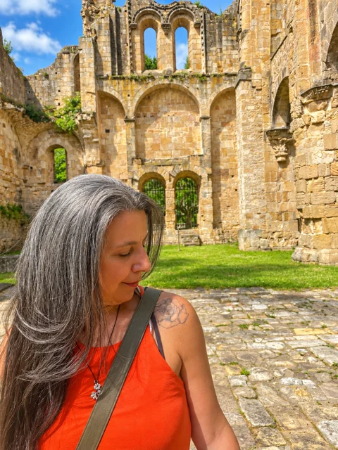 Adriana diante de ruínas de pedra e gramado.