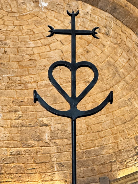 Cruz de Camargue em ferro sobre uma parede de pedra.