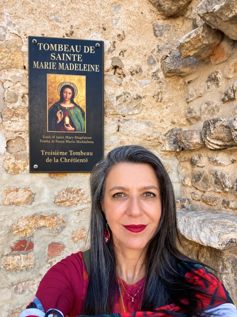 Adriana diante de uma parede de pedra com uma placa.